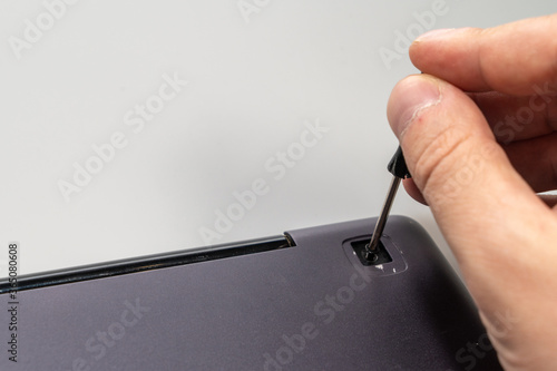male hand with a small screwdriver unscrews the screw on back cover of laptop