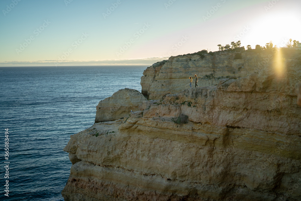 Distant view of couple walking on cliff by sea against clear sky at sunset