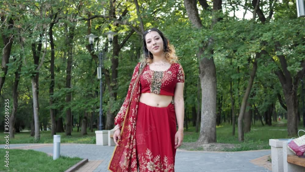Young beautiful woman in Indian ethnic red saree walking in the Park