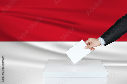 Election in Indonesia. The hand of man putting his vote in the ballot box. Waved Indonesia flag on background. 