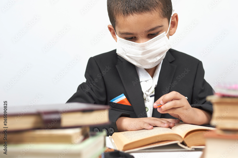 Young schoolboy in face mask doing homework between pile of books. Little kid in black school wear reading book. Back to school after covid-19 pandemic Young schoolboy in face mask doing homework between pile of books. Little kid in black school wear reading book. Back to school after covid-19 pandemic
