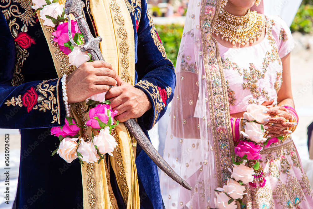 Sikh bride and groom wearing bright traditional clothing on clear sandy beach beneath sunny blue skies