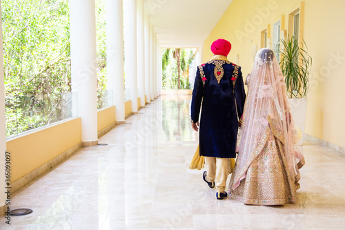 Sikh bride and groom wearing bright traditional clothing on clear sandy beach beneath sunny blue skies