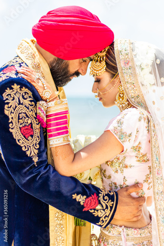 Картината върху платно Sikh bride and groom wearing bright traditional clothing on clear sandy beach be