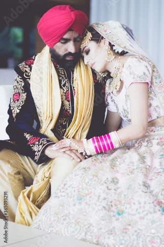 Sikh bride and groom wearing bright traditional clothing on clear sandy beach beneath sunny blue skies
