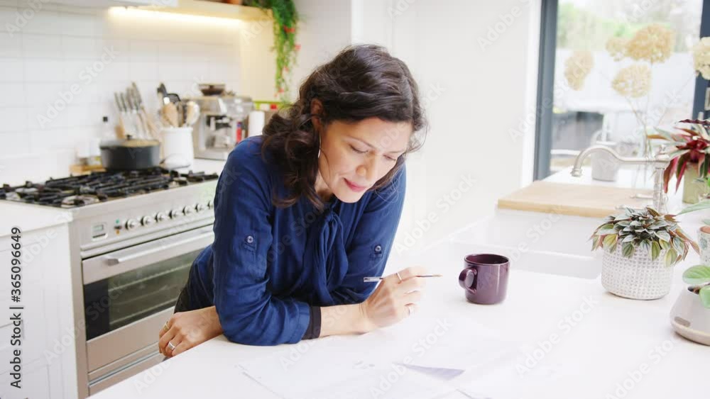 Mature Hispanic woman at home in kitchen reviewing and signing financial documents - shot in slow motion Mature Hispanic woman at home in kitchen reviewing and signing financial documents - shot in slow motion
