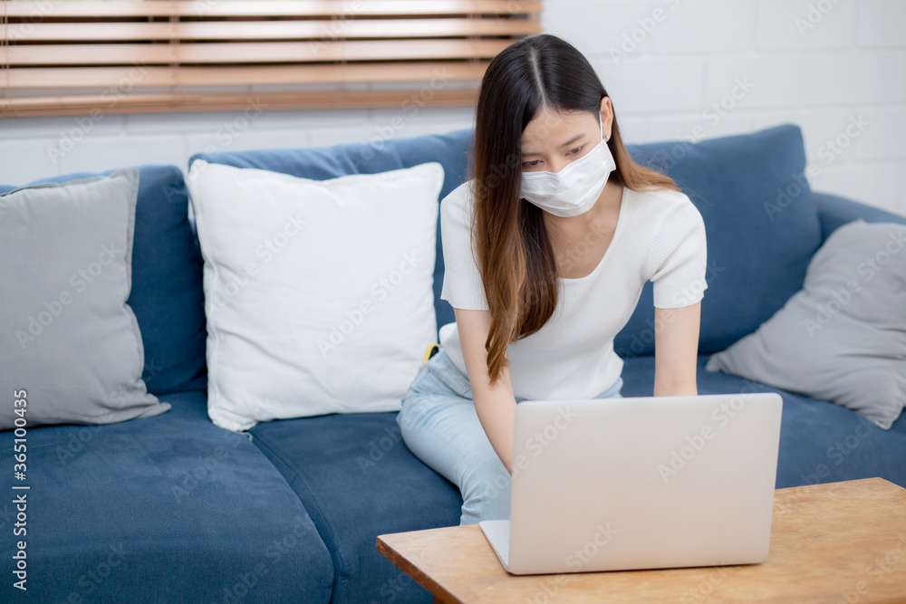 Young asian business woman in face mask work from home on laptop computer online to internet in living room, girl in medical mask and quarantine for pandemic of covid-19, stay home, new normal. Young asian business woman in face mask work from home on laptop computer online to internet in living room, girl in medical mask and quarantine for pandemic of covid-19, stay home, new normal.