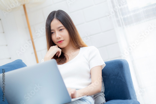 Young asian business woman smile and work from home with laptop computer online to internet on sofa in living room, freelance girl using notebook on couch with comfort, new normal, lifestyle concept.