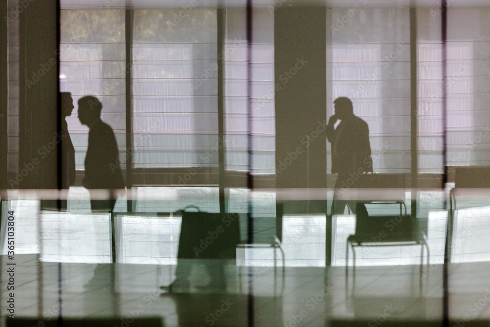 silhouettes of businessmen in building lobby as seen through glass wall at workplace