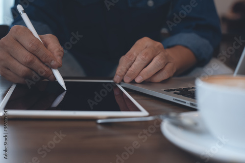 man using stylus pen on digital tablet and working on laptop computer in coffee shop