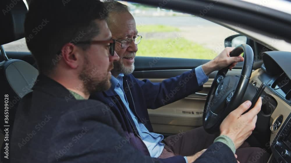 Bearded happy father and son drive luxury car together laughing with funny internet news on smartphone. Business people communication. Motion. Bearded happy father and son drive luxury car together laughing with funny internet news on smartphone. Business people communication. Motion.