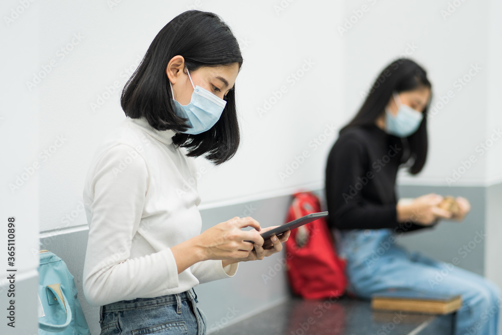 Two female college students wearing mask, reading book and learning while keeping social distance in university campus during COVID-19 pandemic. Stock photo. Two female college students wearing mask, reading book and learning while keeping social distance in university campus during COVID-19 pandemic. Stock photo.