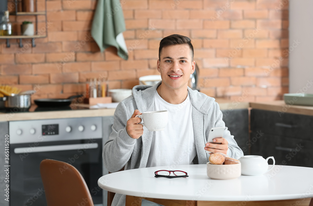 Handsome young man with mobile phone drinking tea at home Handsome young man with mobile phone drinking tea at home
