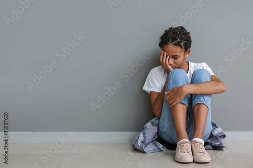 Sad African-American girl sitting near grey wall. Stop racism © Pixel-Shot