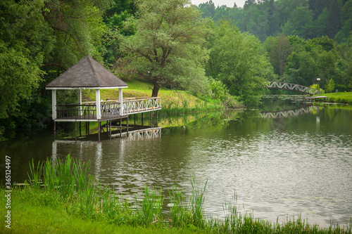 Romantic gazebo on the lake. The gazebo is reflected in the water. Beautiful Park and trees on the river Bank.