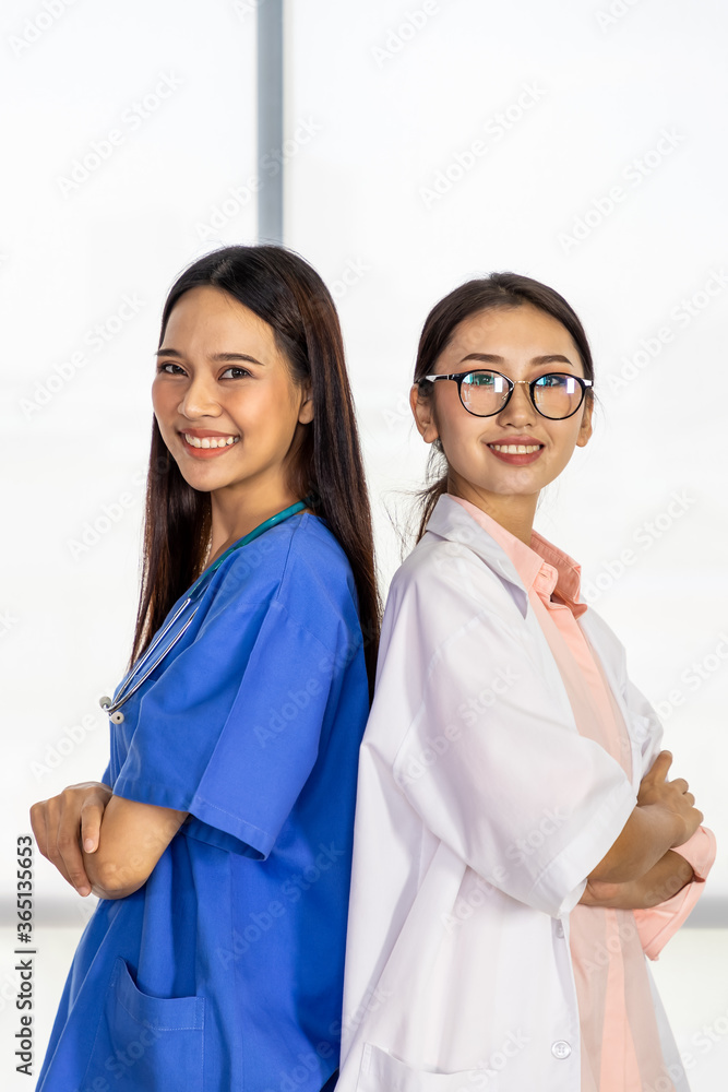 Two confident Asian female medical doctors standing back to back and cross arms; smiling and looking at camera Two confident Asian female medical doctors standing back to back and cross arms; smiling and looking at camera