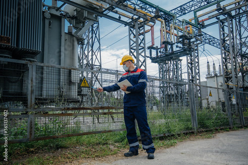 An electrical substation engineer inspects modern high-voltage equipment in a protective mask . Energy. Industry © Anastasija
