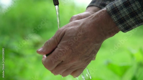 senior man hands wash freshly picked cucumbers under running water against blurry garden slow motion extreme closeup photo