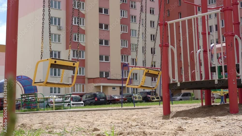 old swings of yellow colour wave on brown rusty chains on local playground against parking lot and building slow motion old swings of yellow colour wave on brown rusty chains on local playground against parking lot and building slow motion
