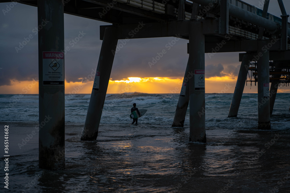 Surfer in the ocean at the pier at sunrise