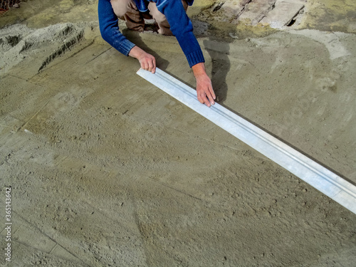 The builder smooths the surface of a dry sand-cement mortar with a long metal plank for laying paving slabs on the site. Male hands level the ground with a large gray ruler. Background with copy space