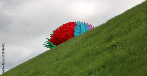Flagi w kolorze flagi Białorusi ułożone w dekoracyjną dużą kulę na pochyłym stoku porośniętym zieloną trawą, na tle szarego nieba