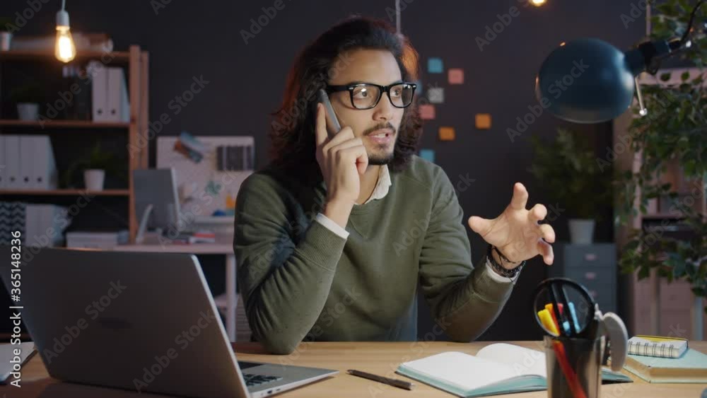 Joyful businessman is speaking on mobile phone in workplace at night smiling discussing business sitting at desk alone. People and overwork concept. Joyful businessman is speaking on mobile phone in workplace at night smiling discussing business sitting at desk alone. People and overwork concept.