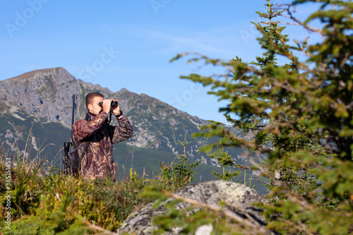The man is on the hunt. Hunting period. Male with gun. Hunter with hunting gun and hunting form to hunt.   In the background high mountains