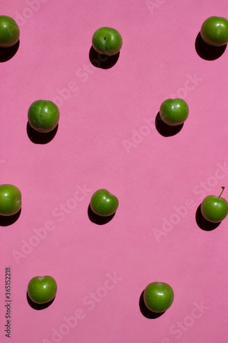 Green plum isolated on pink background. Still life photography. 