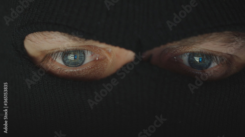 CLOSE UP: Eyes of thief in a black mask (balaclava) before a computer