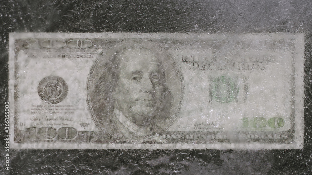 Ice melts on US dollar bill on table - Top view