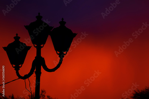 The black outline of a street lamp silhouetted against a heavy red-orange sky with a dark blue cloud. Apocalypse. Horror. Lamppost. Abstract photography. Bad weather. Russia. Saratov.