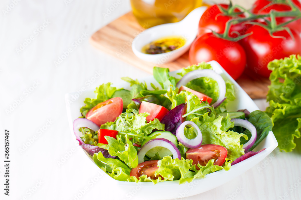 Fresh healthy vegetable salad made of cherry tomato, ruccola, arugula, feta, olives, cucumbers, onion and spices. Greek, Caesar salad in a white bowl on wooden background. Healthy food concept.