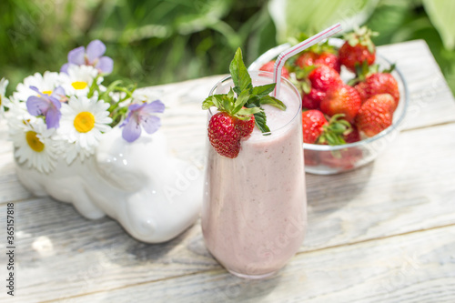 A milkshake with strawberries stands against a light wood background