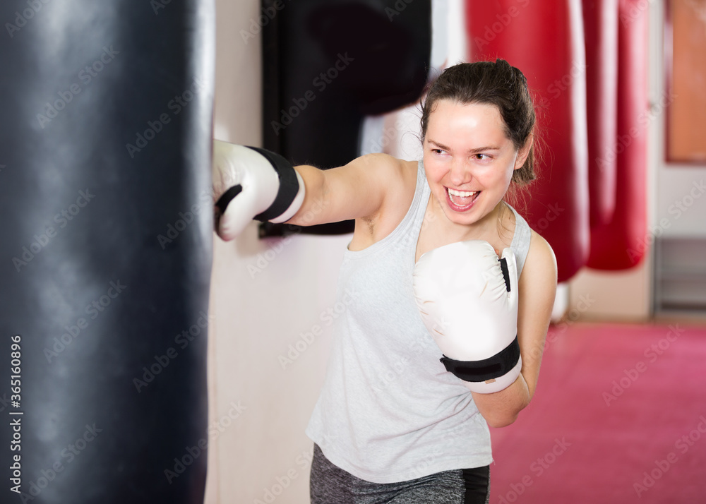 Young woman is beating a boxing bag in the boxing hall.