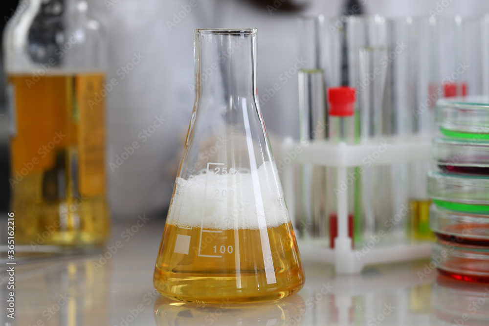 Close-up of yellow alcohol liquid in glass flask. Investigated material on working table. Chemistry and research. Tubes on desktop. Modern investigation and science concept Close-up of yellow alcohol liquid in glass flask. Investigated material on working table. Chemistry and research. Tubes on desktop. Modern investigation and science concept