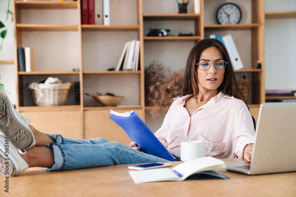 Image of woman working with laptop while sitting with legs on table Image of woman working with laptop while sitting with legs on table