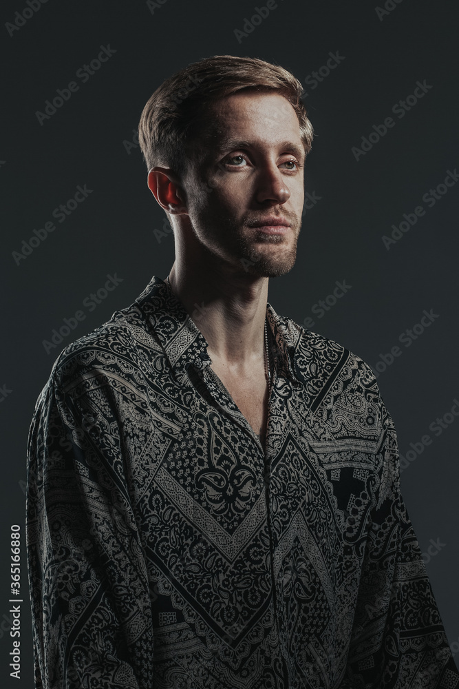 Fototapeta premium Portrait of a handsome caucasian guy in a boho shirt on the black background. Vertical image.