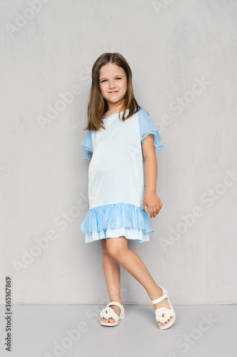 Cute little girl in blue dress and sandals posing near the wall © boomeart