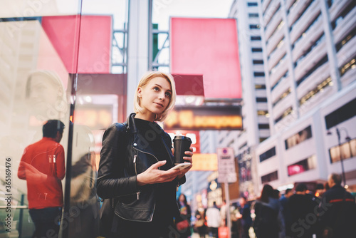 Portrait of pensive female traveler in trendy casual wear having sightseeing tour in modern business district of Chinese city feeling excited of adventures sharing photos in social networks via phone