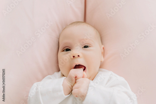 Baby girl lying on the pink pillows and nibbling her fists. Baby 3 months. Newborn sleep. First teeth