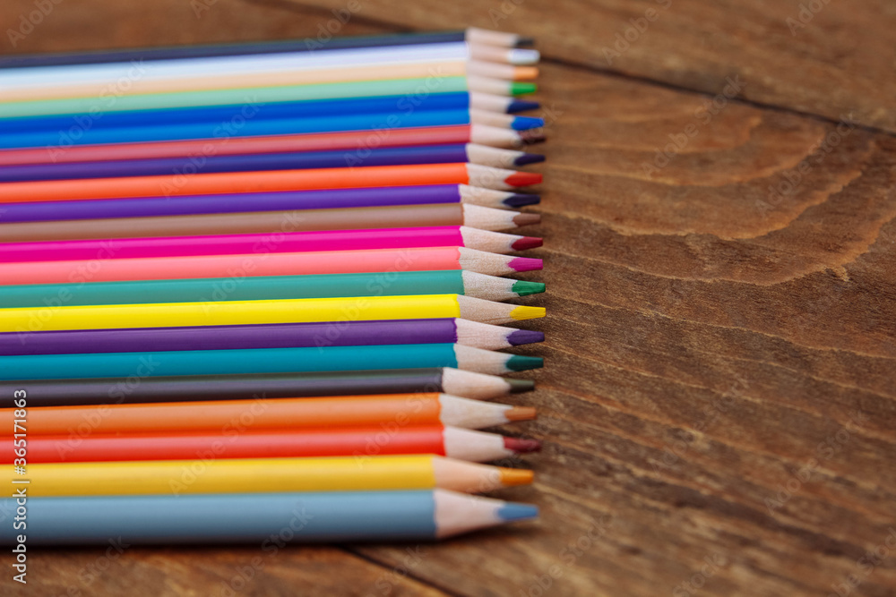 Obraz premium Colored pencils lie in a row on a brown wooden table with an empty space for text, the concept of school education, training and development of children