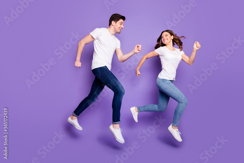 Full size profile photo pretty lady handsome guy jump high sports competition running fast hurry finish line couple race wear casual t-shirts jeans shoes isolated purple color background