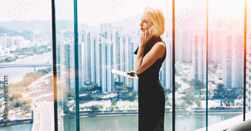 Woman owner of successful enterprise with touch pad in hand having serious conversation with manager about the loss of new clients, while is standing in skyscraper office interior during business trip photo