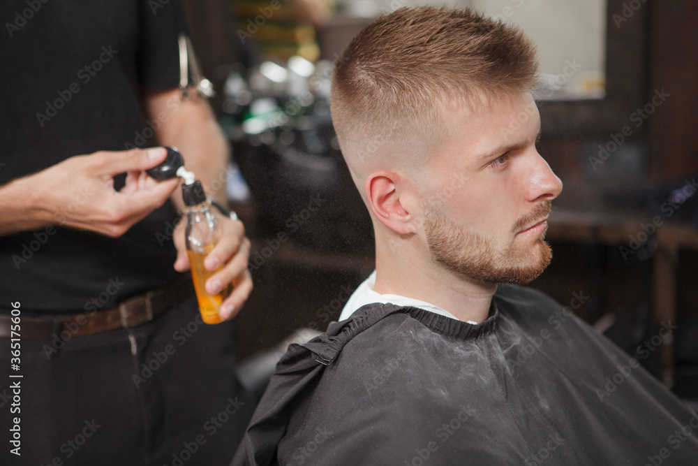 Unrecognizable barber spraying cologne on his male customer after