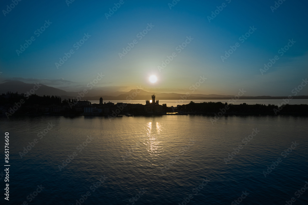 Naklejka premium Sunrise over Sirmione, Lake Garda Italy. Blue sky, trail from the sun on the water. Aerial view