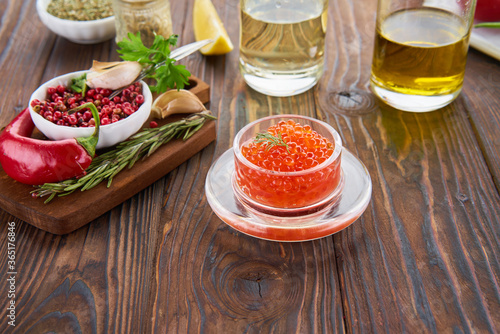Composition with red caviar in the glass jar on the wooden table and ingredients for cooking