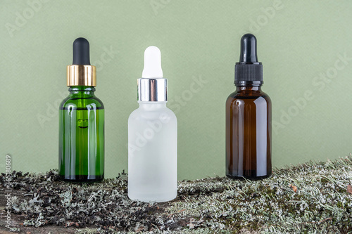 Three brown  green  white glass bottles with serum  essential oil or other cosmetic product on tree bark covered with moss against green background. Natural Organic Spa Cosmetic Beauty concept