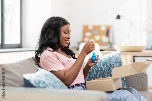 delivery, shipping and people concept - happy young african american woman opening parcel box with cosmetcis at home