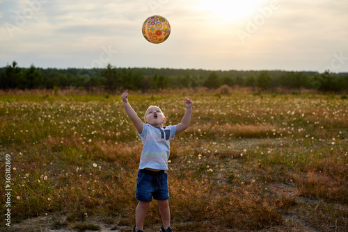 Little happy boy plays with a ball on a summer meadow.